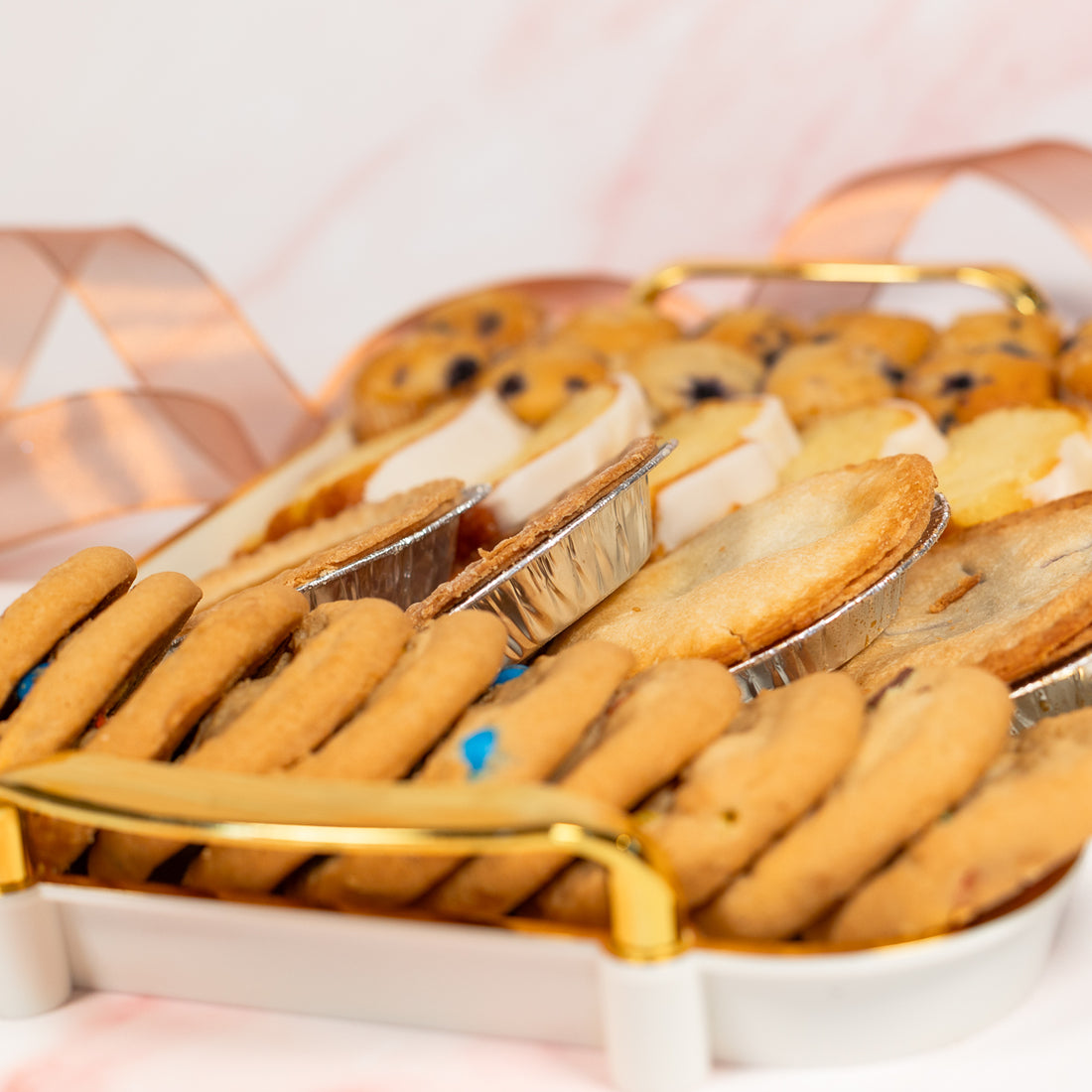 Mini pies and cookies in a glass display case with a pink background