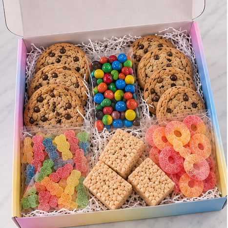 A boxed assorted cookie and candy gift set displayed from above in an open pastel gradient box. The set includes chocolate chip cookies, M&M&