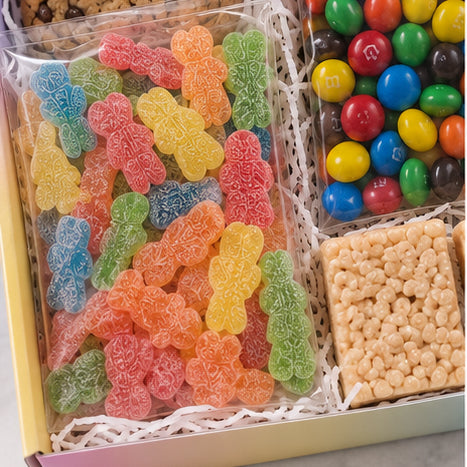 A gift box filled with assorted packaged candies, including a large clear bag of colorful gummy bears, a bag of M&M&