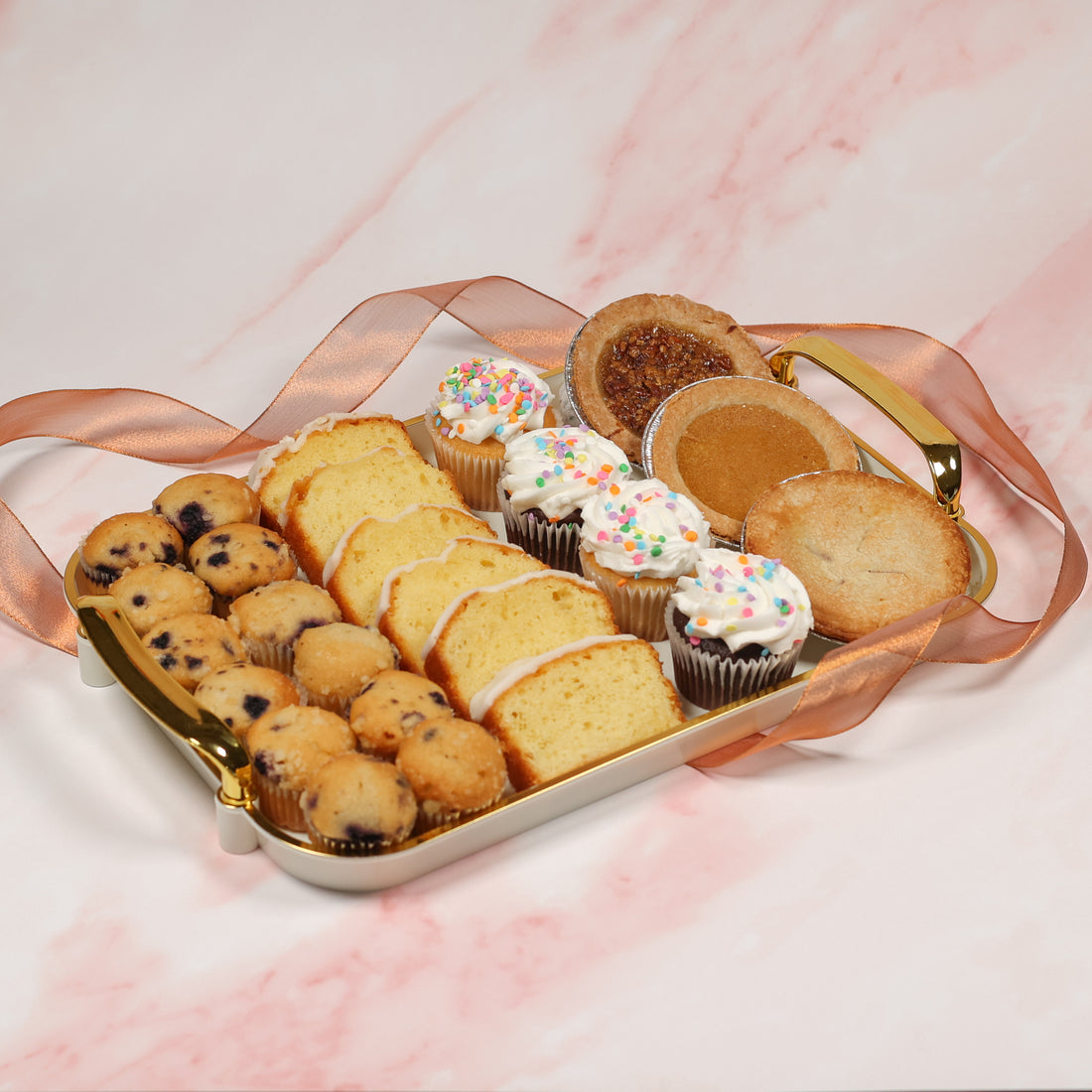 Assorted pastries including muffins, cupcakes, and cookies on a decorative tray with a pink and white background.
