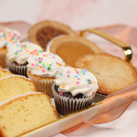 Assorted baked goods including cupcakes with white frosting and colorful sprinkles on a tray.