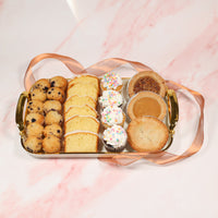 Assorted pastries including cookies, cakes, and cupcakes on a decorative tray with a pink background.
