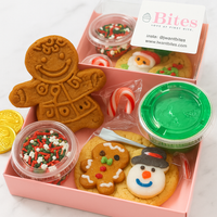 Gingerbread-themed cookie kit with a gingerbread man cookie, snowman cookie, and decorating supplies in a pink box.